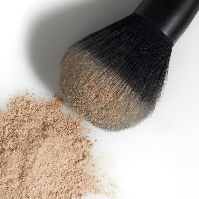Schwarzer Make Up Pinsel und loser Mineralpuder auf weißem Grund